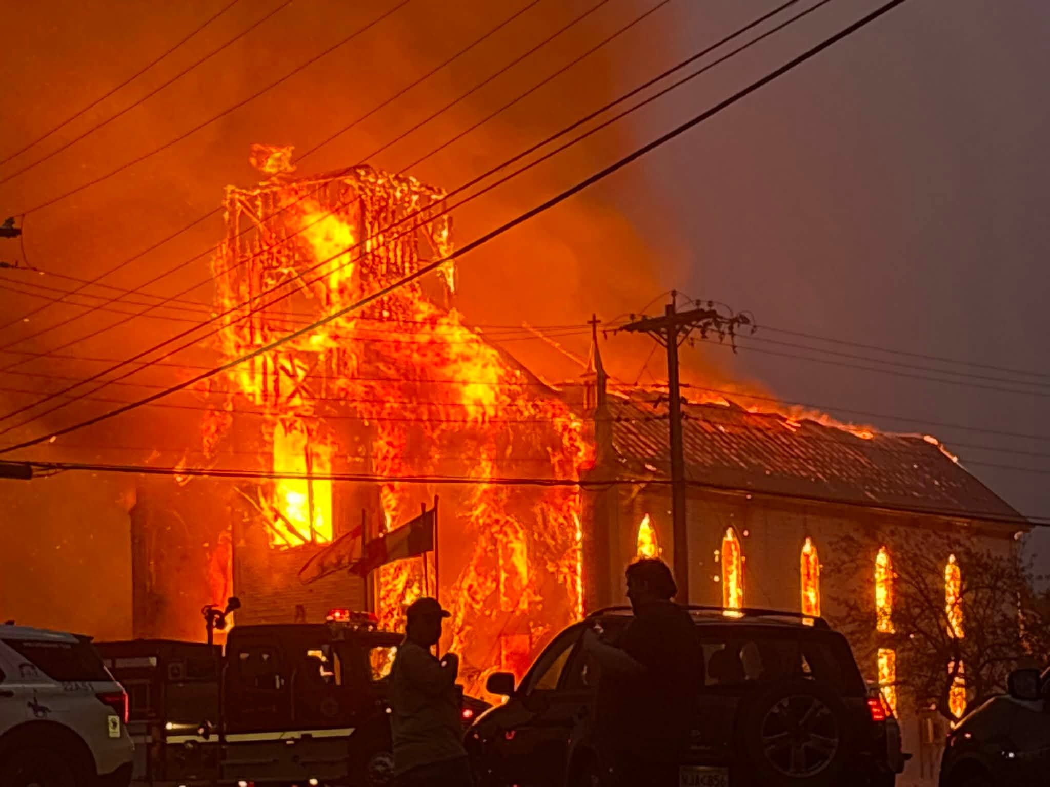 Bystanders watch as Saint-Simon Catholic Church burns in New Brunswick, Canada, on Aug. 24, 2026. Police later arrested a 68-year-old man in connection with the fire. | Credit: Yvonne Chiasson